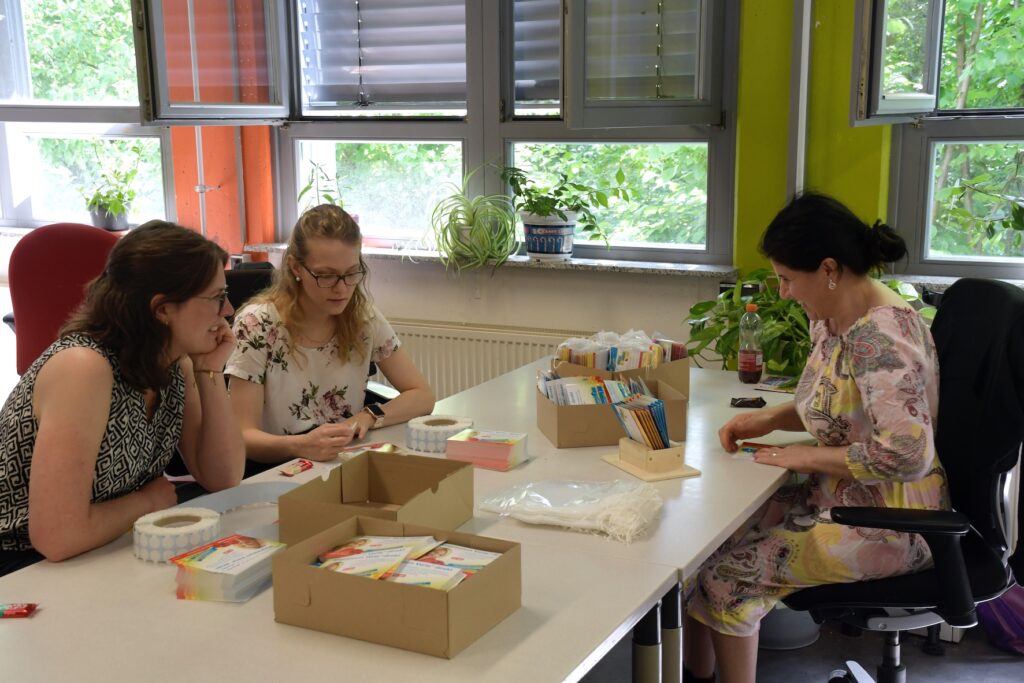 Mitarbeiter von Ipsen Pharma bereiten einen Briefversand mit einer Klientin der Stiftung Pfennigparade vor.